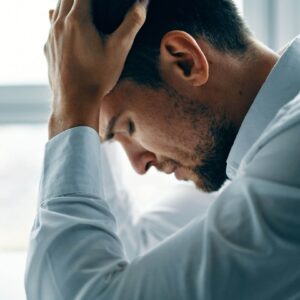 Shows a man looking stressed out with his head in his hands. Represents how a therapist specializing in trauma in fort worth and trauma therapy in Fort Worth, TX can help you work through your trauma.