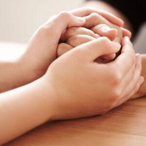 Two hands clasped together in support, symbolizing connection and healing. Trauma therapy in Fort Worth with a Fort Worth trauma therapist can help you navigate past wounds.