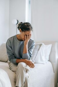 A distressed woman sits on the edge of a bed, resting her head in her hand, struggling with emotional pain. Relationship trauma can leave lasting scars, making it hard to feel safe in future connections. Seeking trauma therapy in Fort Worth, TX with a trauma therapist in Fort Worth, TX can help process the impact and begin the healing journey.