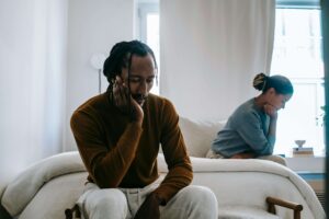 A distressed couple sits apart, struggling with emotional disconnect. A therapist for relationship trauma in Fort Worth, TX can help navigate healing through trauma therapy in Fort Worth, TX, fostering trust and deeper connection.