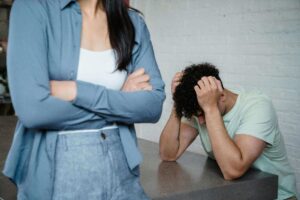 Shows a man with his head down with a woman is standing closer to the camera with her arms crossed over her chest. Represents how a fort worth trauma therapist paired with trauma counseling in fort worth can help you acknowledge your trauma within your relationship.